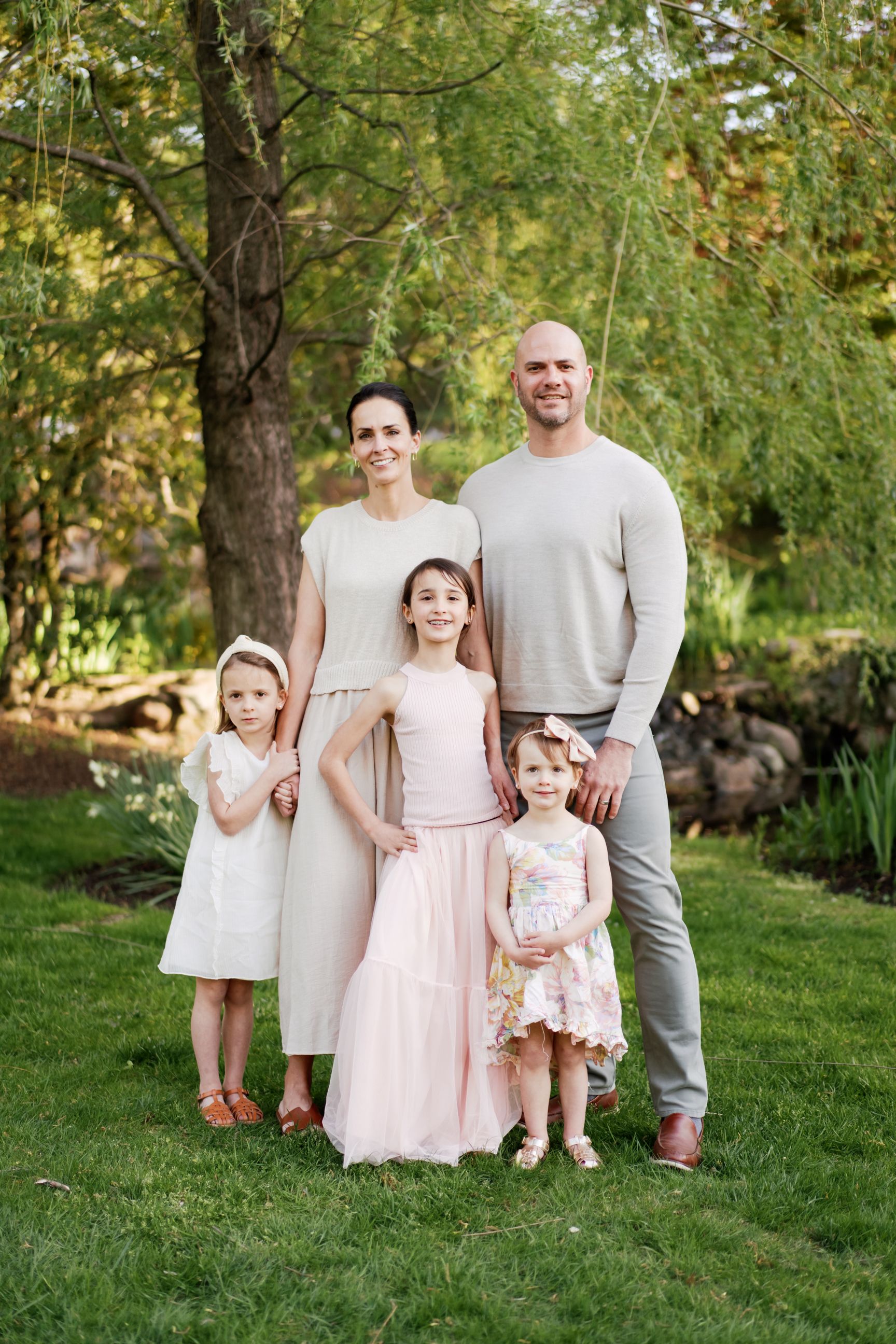 A family wearing coordinated pastel outfits poses together outdoors in a natural spring garden setting.