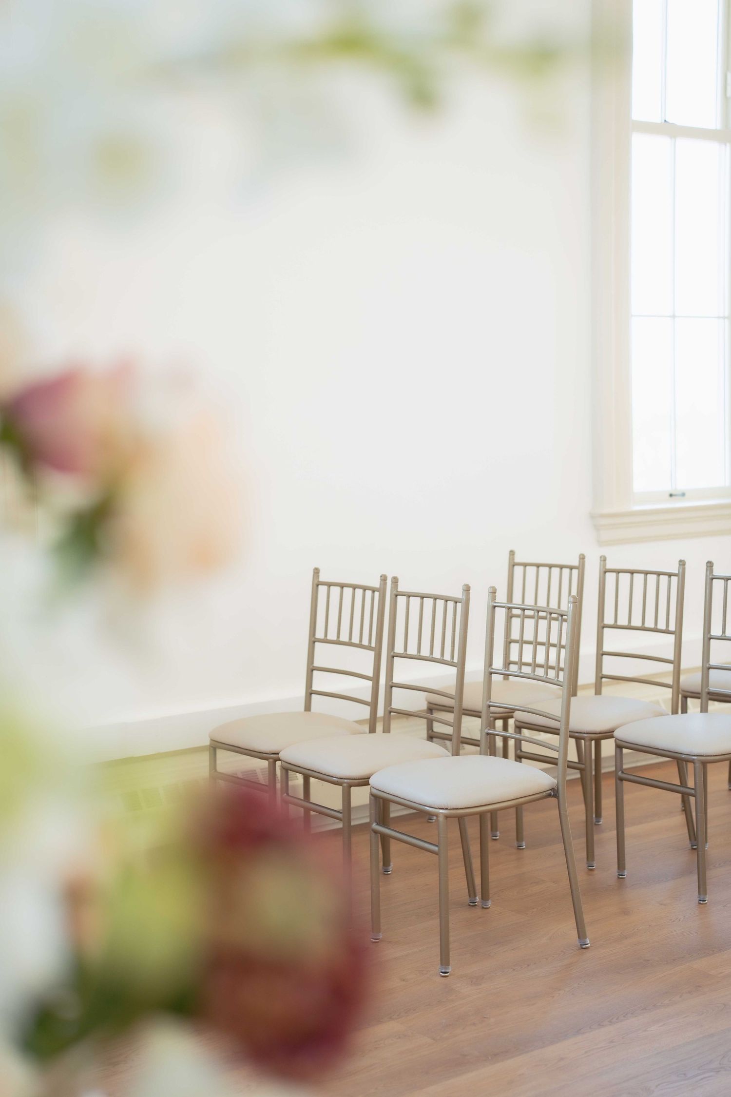 Gold chiavari chairs arranged in rows in a light-filled room with soft floral accents. Events at Ethereal Courthouse Square