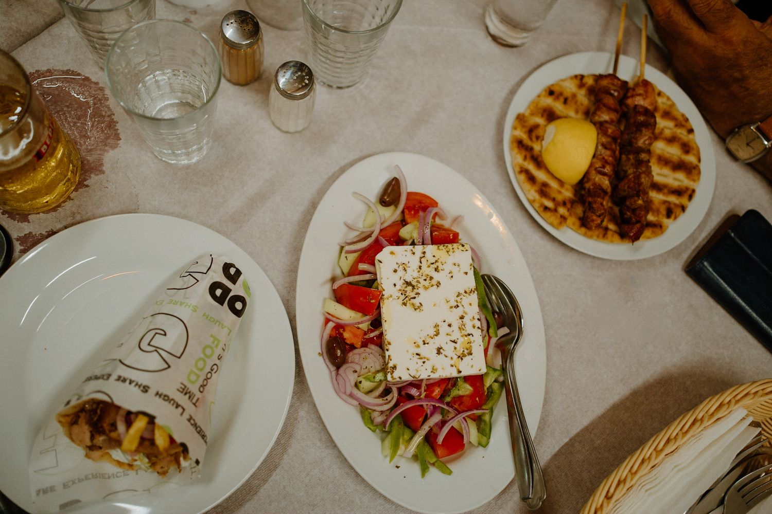 Table setting with Greek salad topped with feta cheese, grilled waffle plate, and drinks at a restaurant.