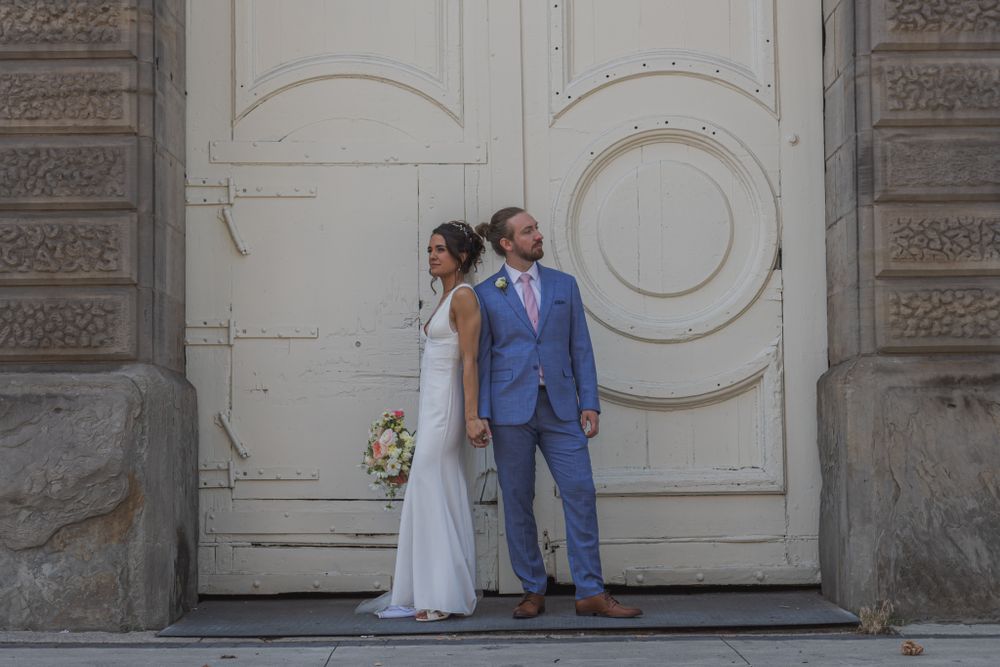 A couple poses in front of an ornate white door during a wedding photoshoot.