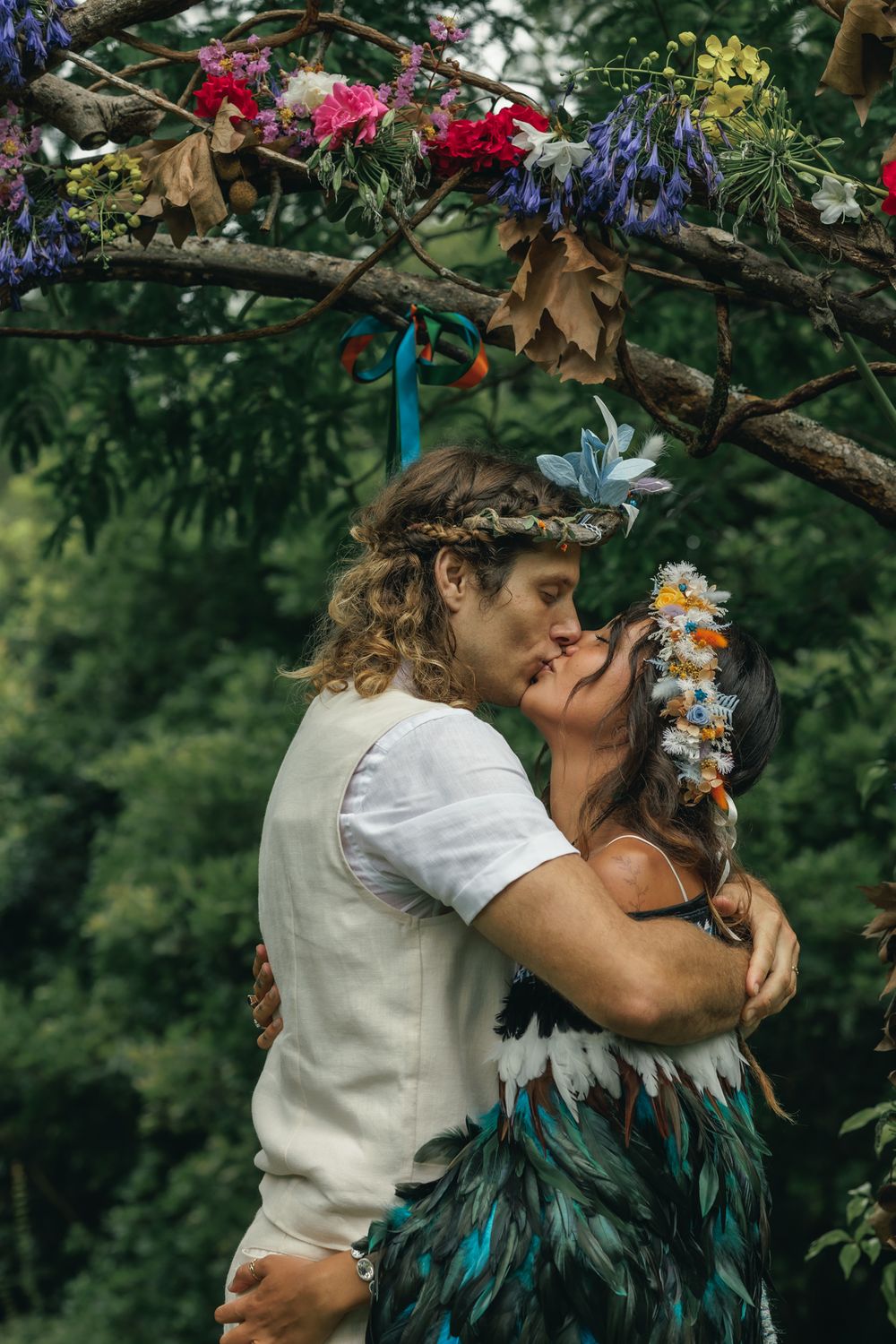 A romantic embrace under a floral arch with colorful blooms and branches in a garden setting.