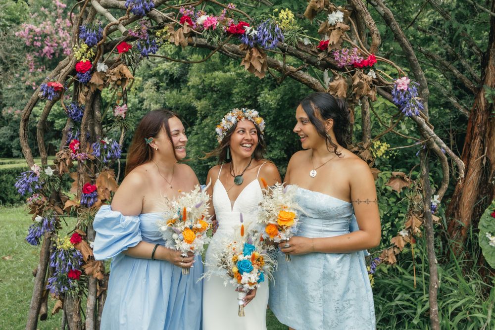 Three bridesmaids in light blue dresses pose together holding bouquets in a garden setting.