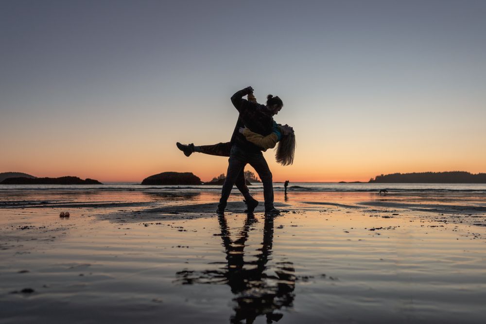 Silhouettes of a couple playing on a beach at sunset with reflections in the water.