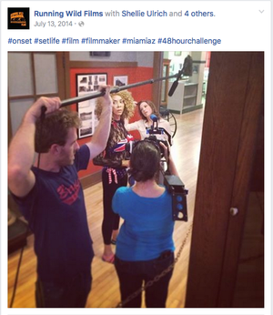 Behind the scenes photo of a film crew working on set with hashtags about filmmaking.