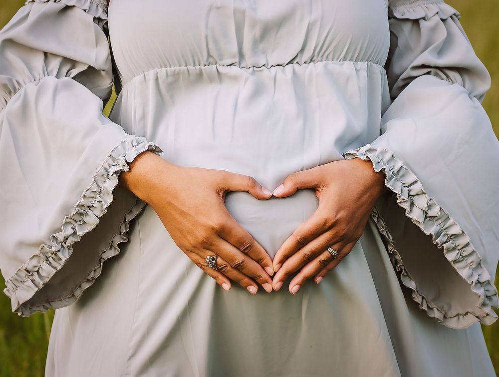 Hands forming heart shape over a light gray dress with ruffled sleeves.