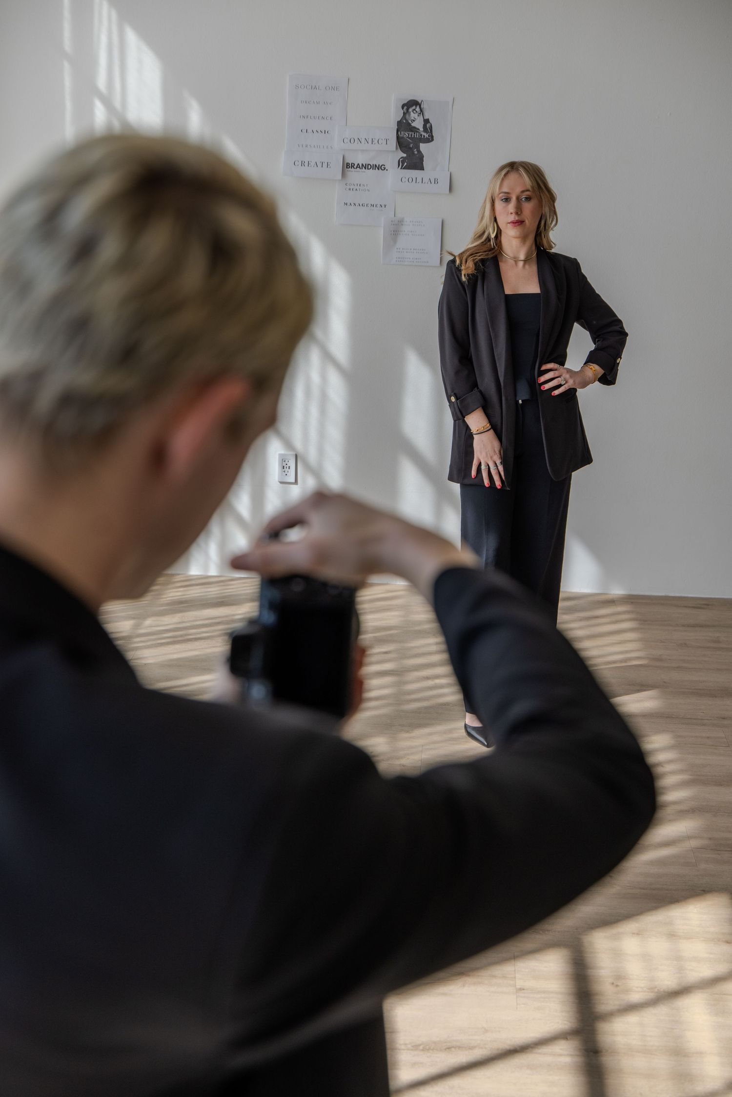 Professional photographer wearing black suit holds DSLR camera mounted on stabilizing grip in dimly lit room with red wall.