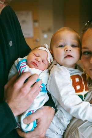 A tiny newborn baby wearing a white onesie being cradled gently.