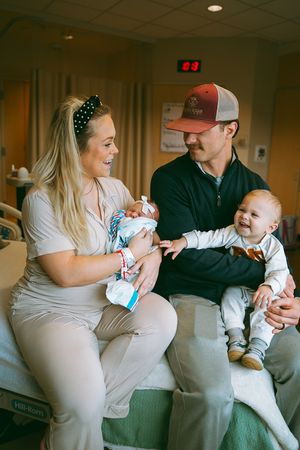 A couple sits on a couch in a hospital room spending time with their newborn.