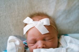 Newborn with white medical tape resting peacefully in hospital.
