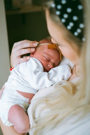 Close-up view of a newborn baby swaddled in white blankets being gently held.