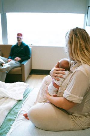 Family bonding with newborn baby while resting on hospital bed.