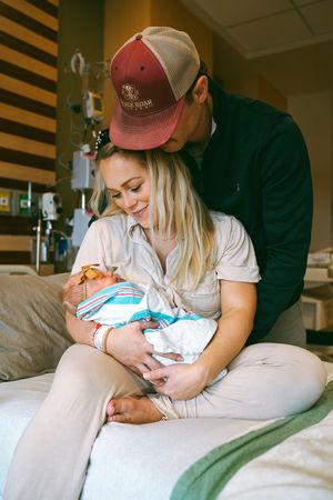 Parents cuddle with their newborn baby on hospital bed during first moments together.