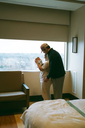 Emotional first moments between parents and newborn in hospital room with large windows.