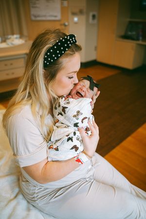 Mother in white shirt holding and bonding with newborn baby wearing patterned onesie.