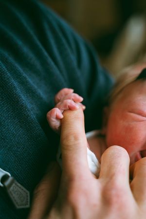 A tiny newborn baby's hand grasps an adult finger in a tender moment.