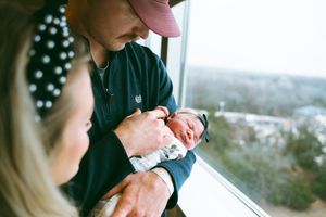 A newborn baby being cradled near a window with a city view in the background.