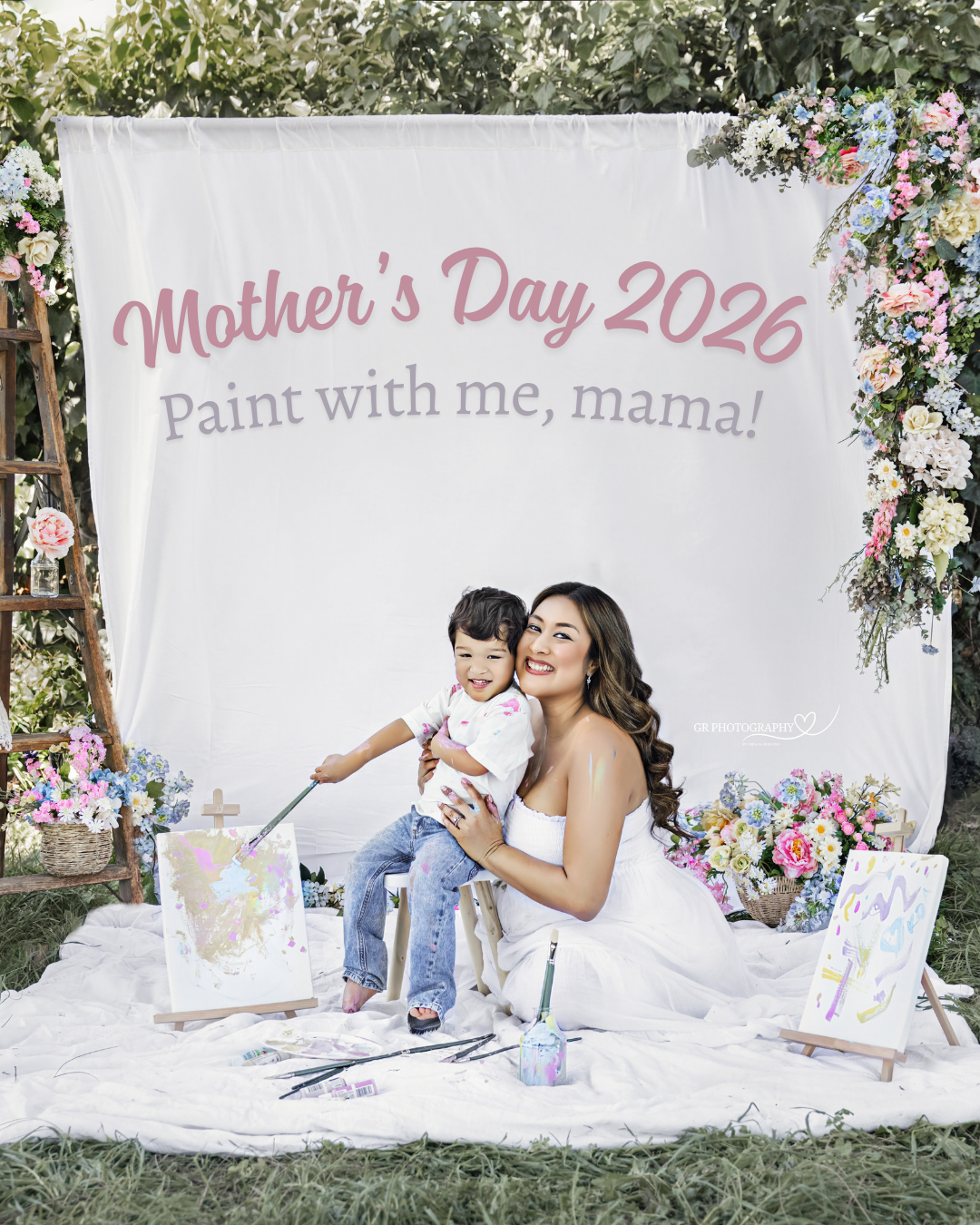 Mother and daughter in matching pink gowns pose beneath a luxurious floral arch with roses and hydrangeas.