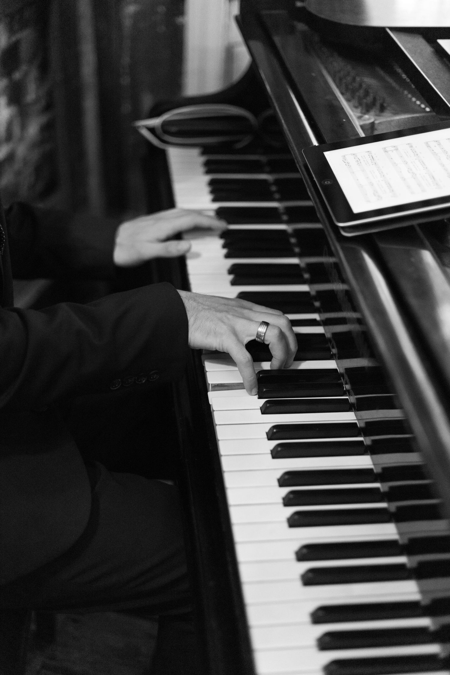 Close-up black and white photo of hands playing piano with sheet music visible.