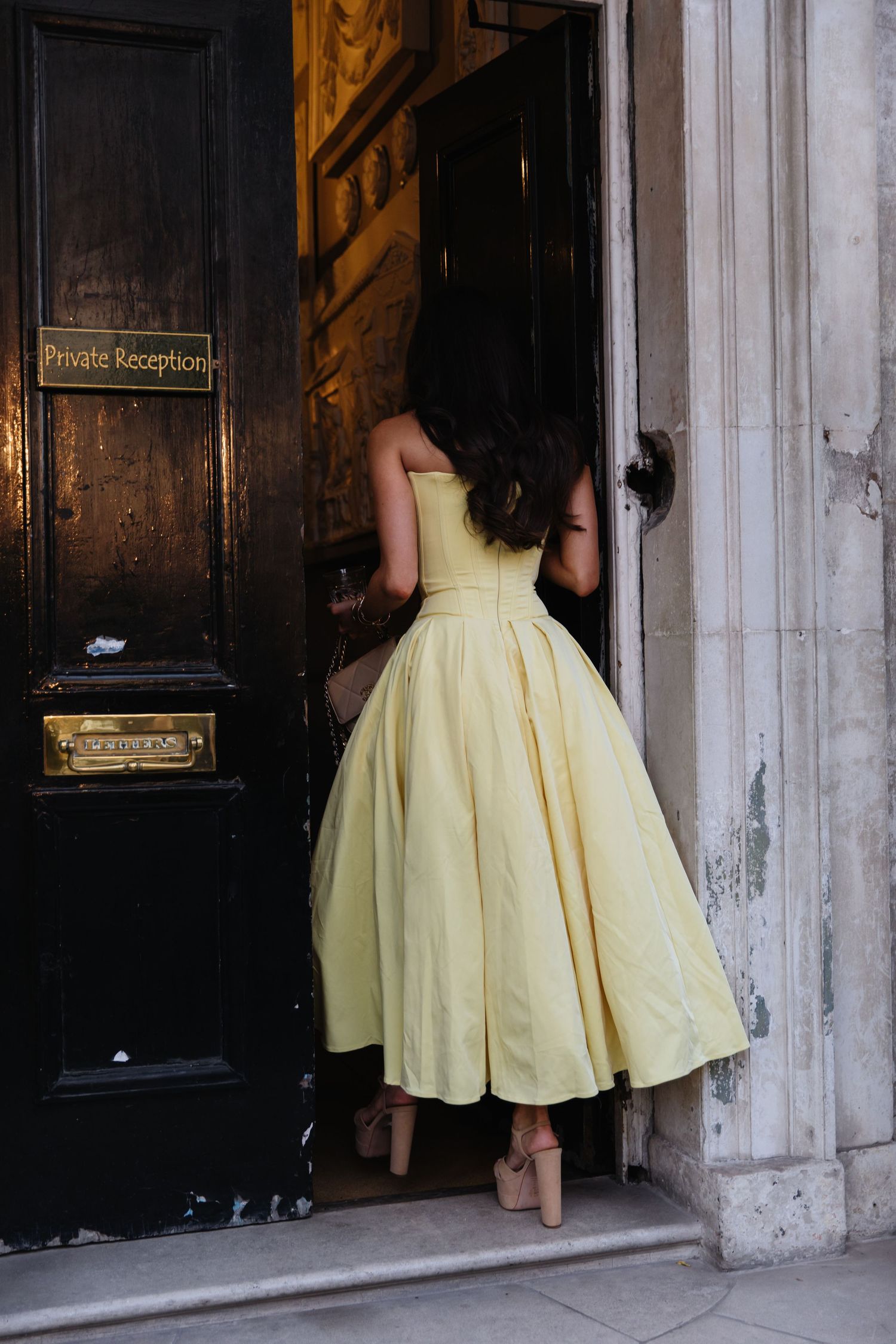 Person wearing yellow vintage-style dress entering through dark wooden doorway.