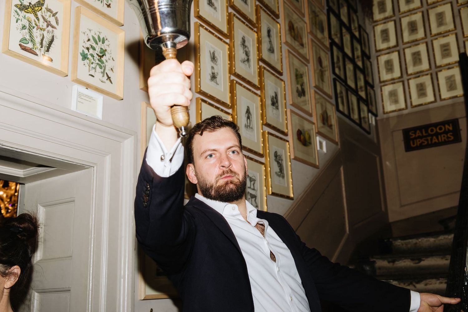 Person in formal attire raising a glass at an event with framed artwork on walls.