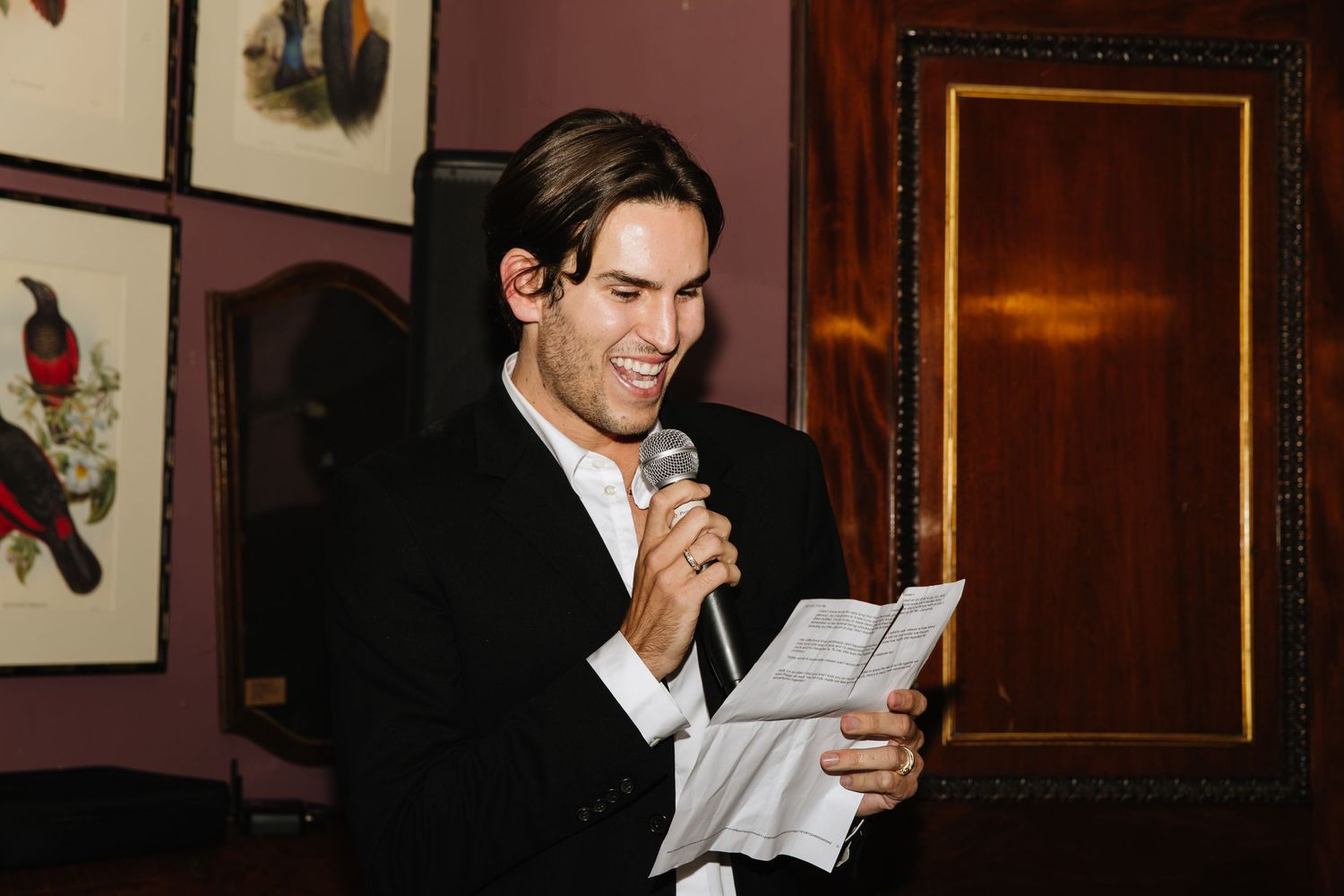 Person in black suit reading from papers at formal event.