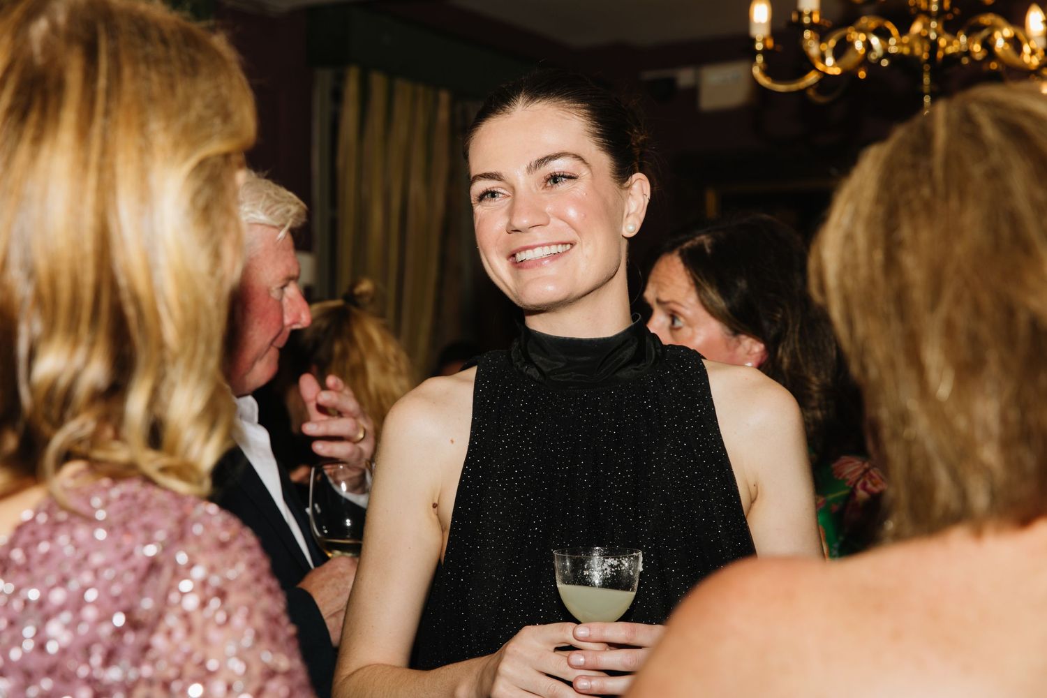 Guests enjoying conversation and drinks at an elegant evening reception with chandeliers.