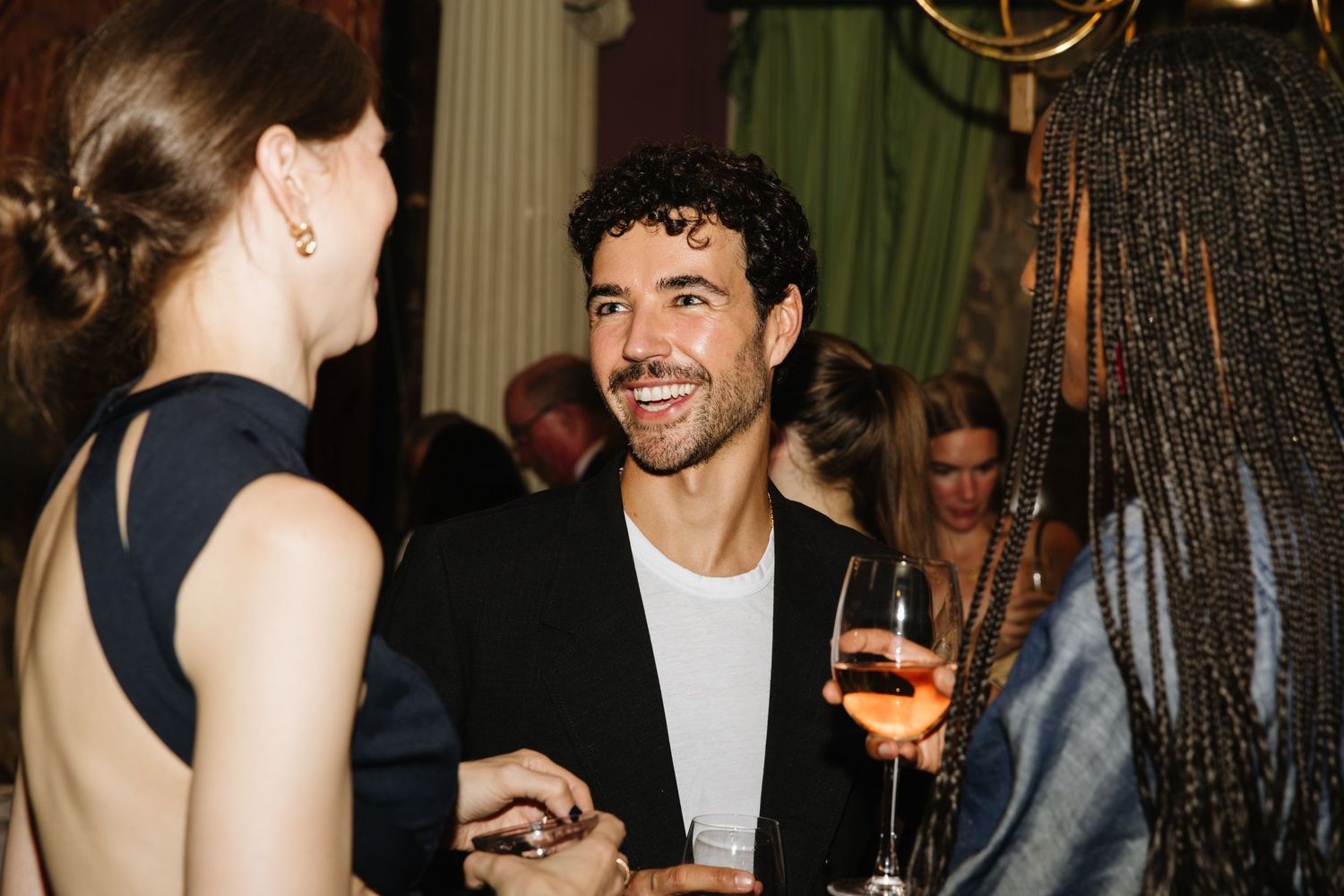 Party guests engaged in lively conversation while holding drinks at an elegant indoor event.