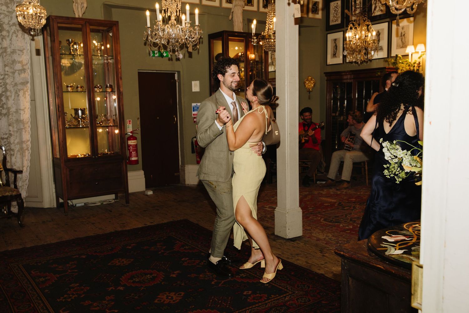 Couples dancing in an elegantly lit room with vintage decor and chandeliers.