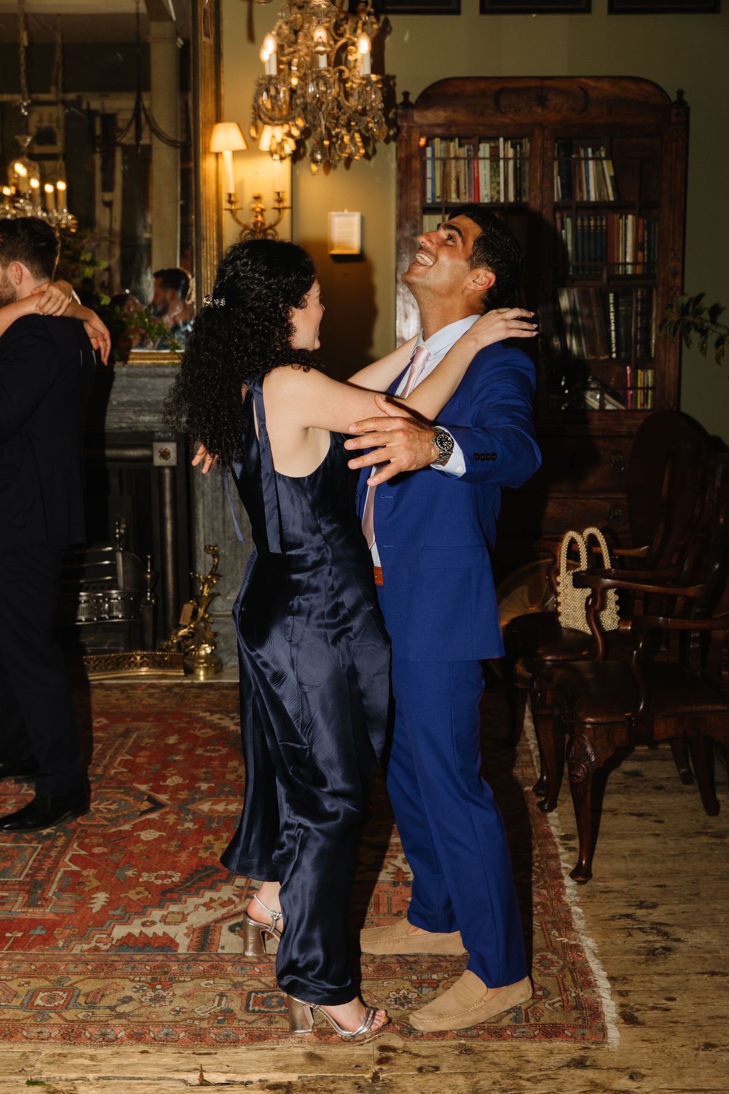 Couple dancing joyfully in a luxurious room with chandeliers and vintage furnishings.