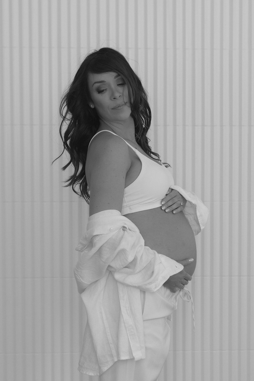 Woman in flowing white top poses artistically against white striped wall in black and white photo series.