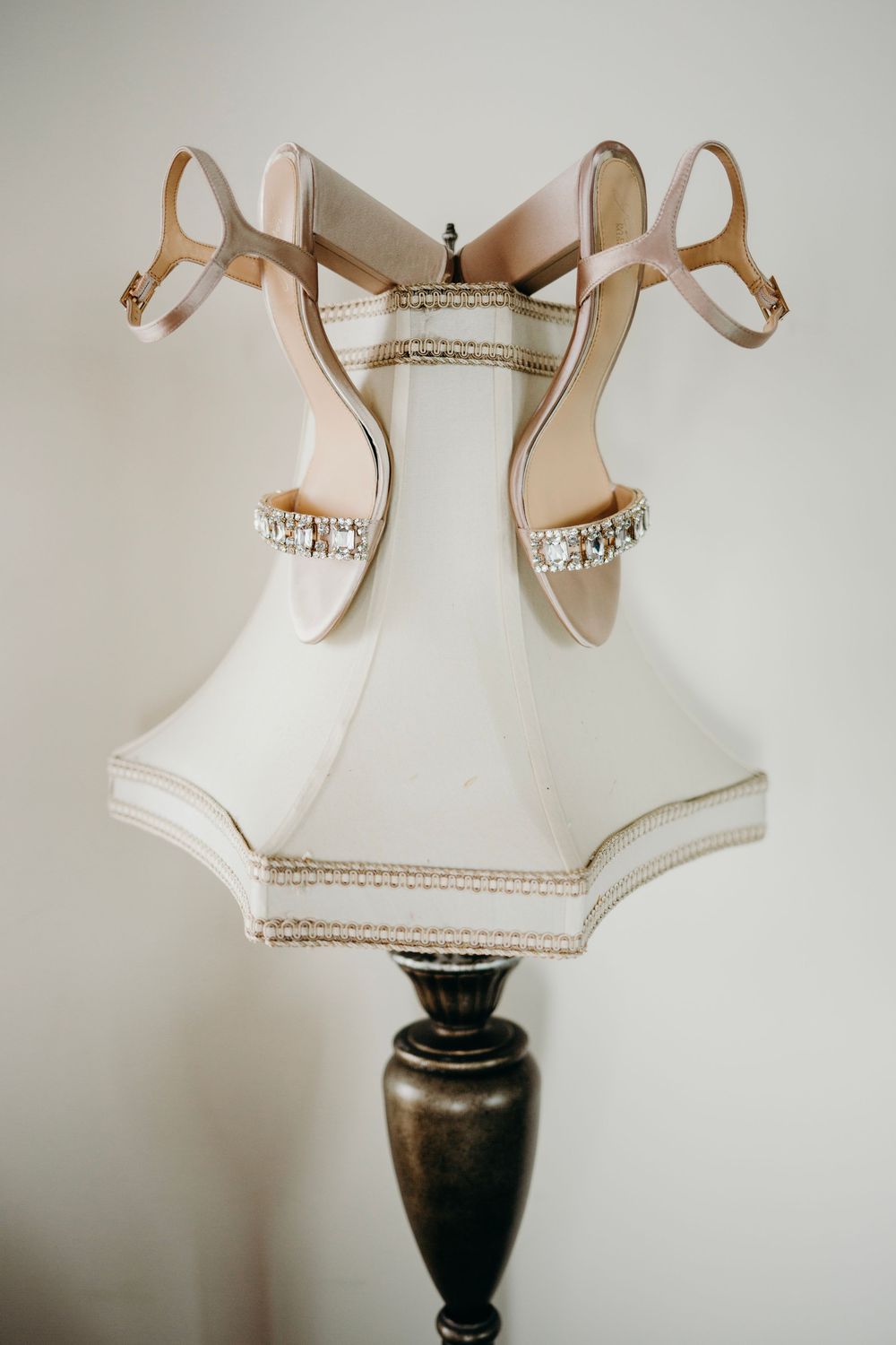 Elegant white bridal shoes with crystal embellishments displayed on dark vase-shaped pedestals against neutral background.