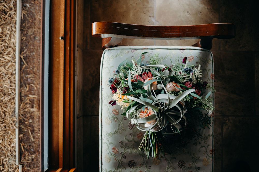 A vintage ornate gold frame hangs on a dark wall with floral arrangements displayed in glass vases nearby.