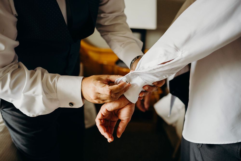 Close-up view of hands adjusting a white dress shirt cuff with cufflinks during formal attire preparation.