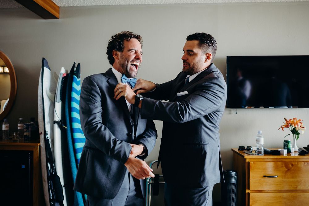 Two people in formal suits help each other adjust their attire while getting ready for a special occasion.