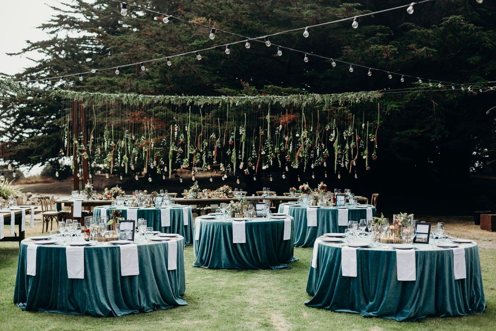 Outdoor wedding reception setup with teal tablecloths and string lights under tall trees creating an elegant forest atmosphere.