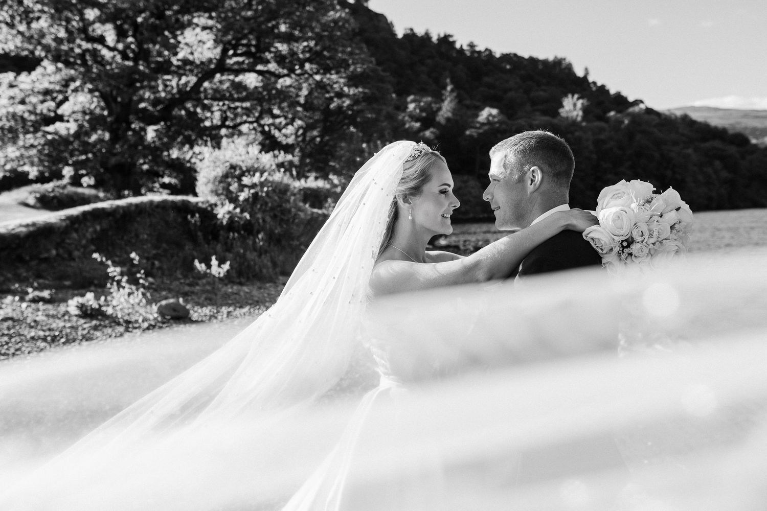 Black and white wedding photo series showing couple in formal attire embracing outdoors with scenic mountain backdrop.
