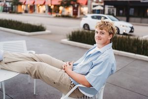 A person in light blue clothing sits on a bench in an outdoor setting during daytime.