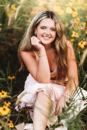Young woman in floral dress smiling among yellow wildflowers in a sunlit field.