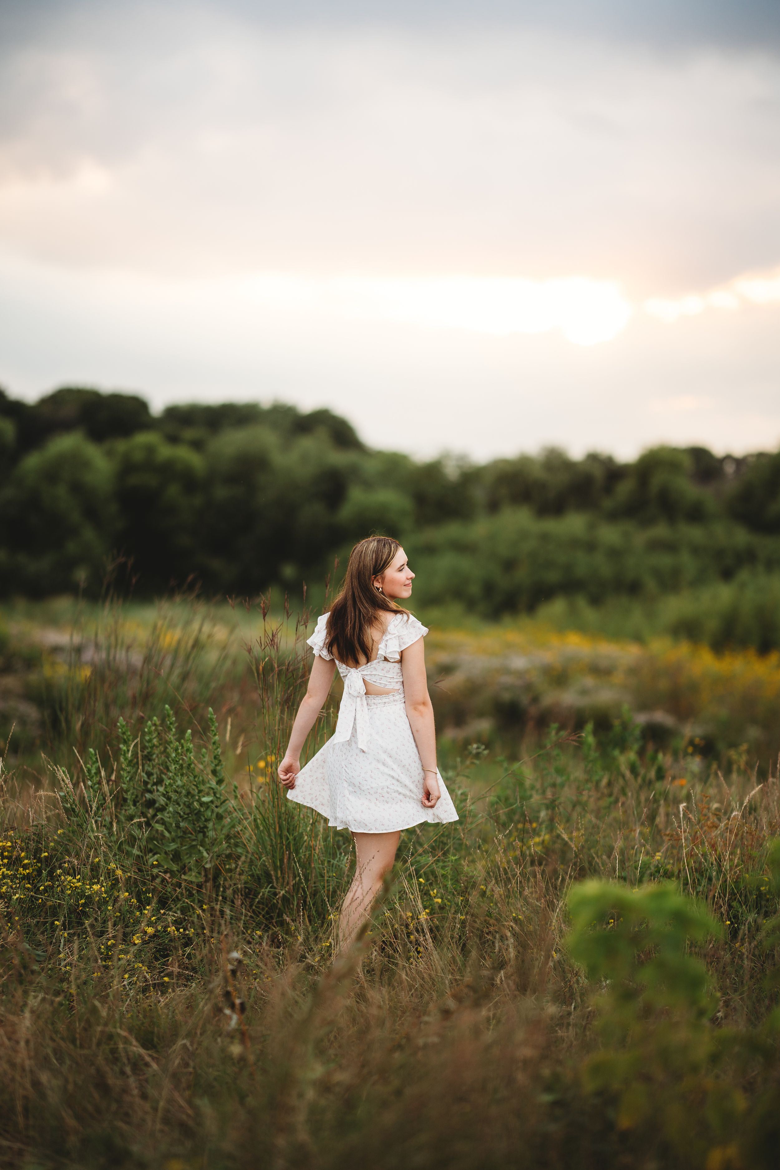 A young girl in a white dress twirls through a golden meadow at sunset creating a dreamy summer scene.