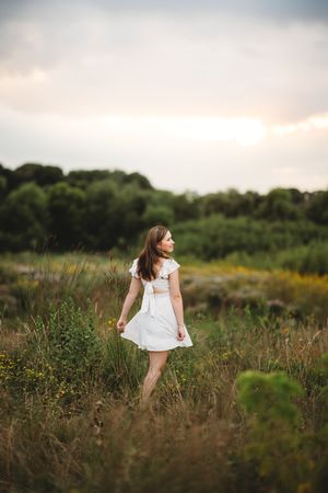 A young girl in a white dress twirls through a golden meadow at sunset creating a dreamy summer scene.