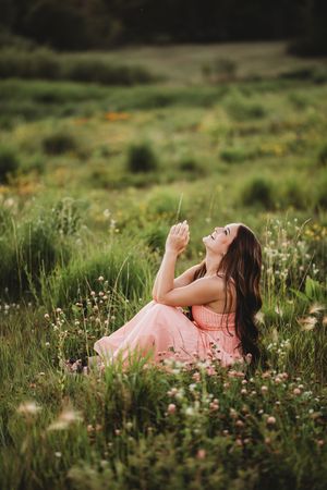 A woman in a pink dress lies peacefully among wildflowers in a lush green meadow during golden hour.