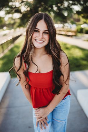 A series of outdoor portraits showing someone in a bright red tank top and blue jeans against a sunny natural background.