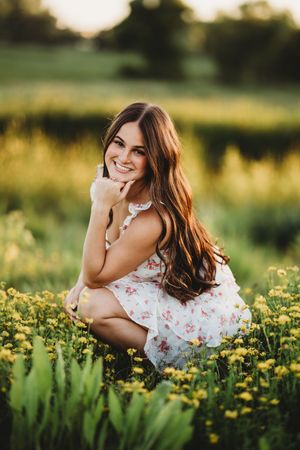 A person in a floral dress lies in a field of yellow wildflowers during golden hour.
