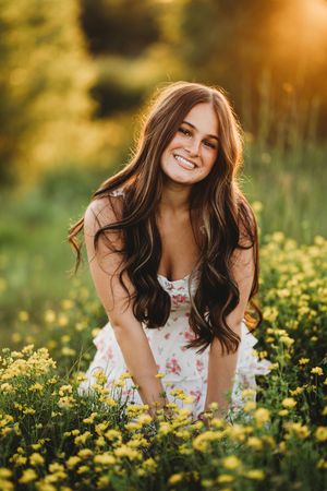 A woman in a floral dress lies in a field of yellow wildflowers during golden hour.