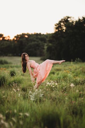 A person in a flowing pink dress dances gracefully through a wildflower meadow at sunset.