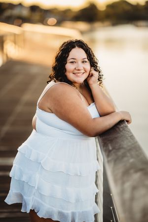 A person in a white ruffled dress poses outdoors during golden hour with soft bokeh lighting in the background.