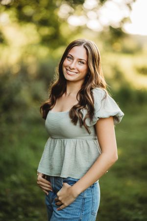 A person wearing a sage green puff sleeve top and blue jeans poses outdoors in soft natural lighting.