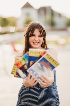 A series of photos showing someone in striped overalls holding and displaying multiple books with a bright smile.