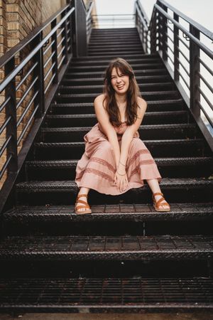 A person in a pink dress sits and smiles on dark metal stairs in a series of candid lifestyle portraits.
