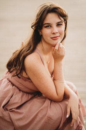 A figure in a dusty rose colored dress poses gracefully against a light neutral background in a photo series.
